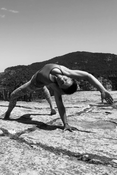 Yoga Frau Müller übt seitliche Yoga-Pose auf Felsplateau mit Blick auf bewaldete Hügel.