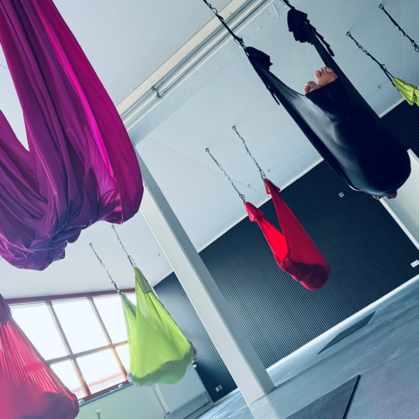 Yoga Helle Yogahalle mit bunten Tüchern für Aerial Yoga, eine Person hängt kopfüber.