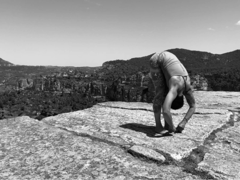 Yoga Frau Müller beugt sich in Vorwärtsdehnung auf Felsplateau mit Blick auf Felslandschaft.