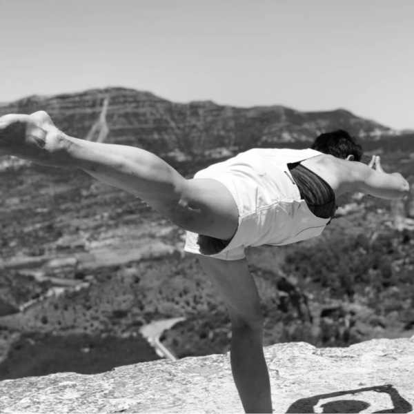 Yoga Frau Müller balanciert in Yoga-Pose auf Felsplateau mit Blick ins weite Talpanorama.
