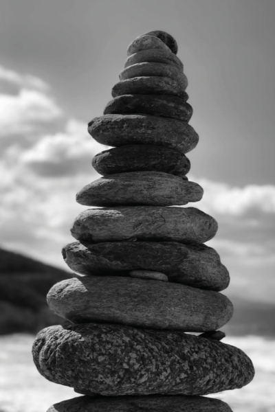 Yoga Hoher Turm aus flach geschichteten Steinen vor bewölktem Himmel am Meer.