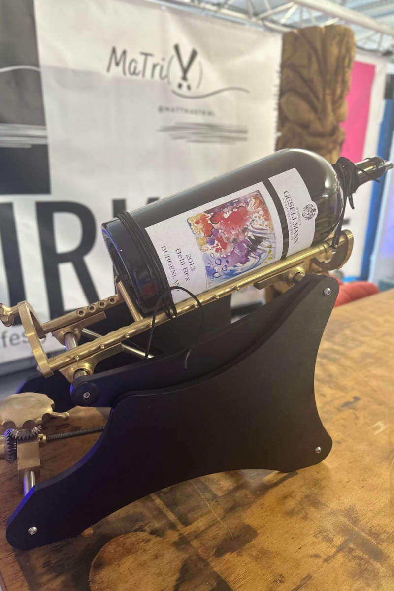 Dekanter Große Weinflasche des Weinguts Giesellmann in antiker Kipphalterung (Dekanter) auf Holztisch, im Hintergrund MaTriX Banner.