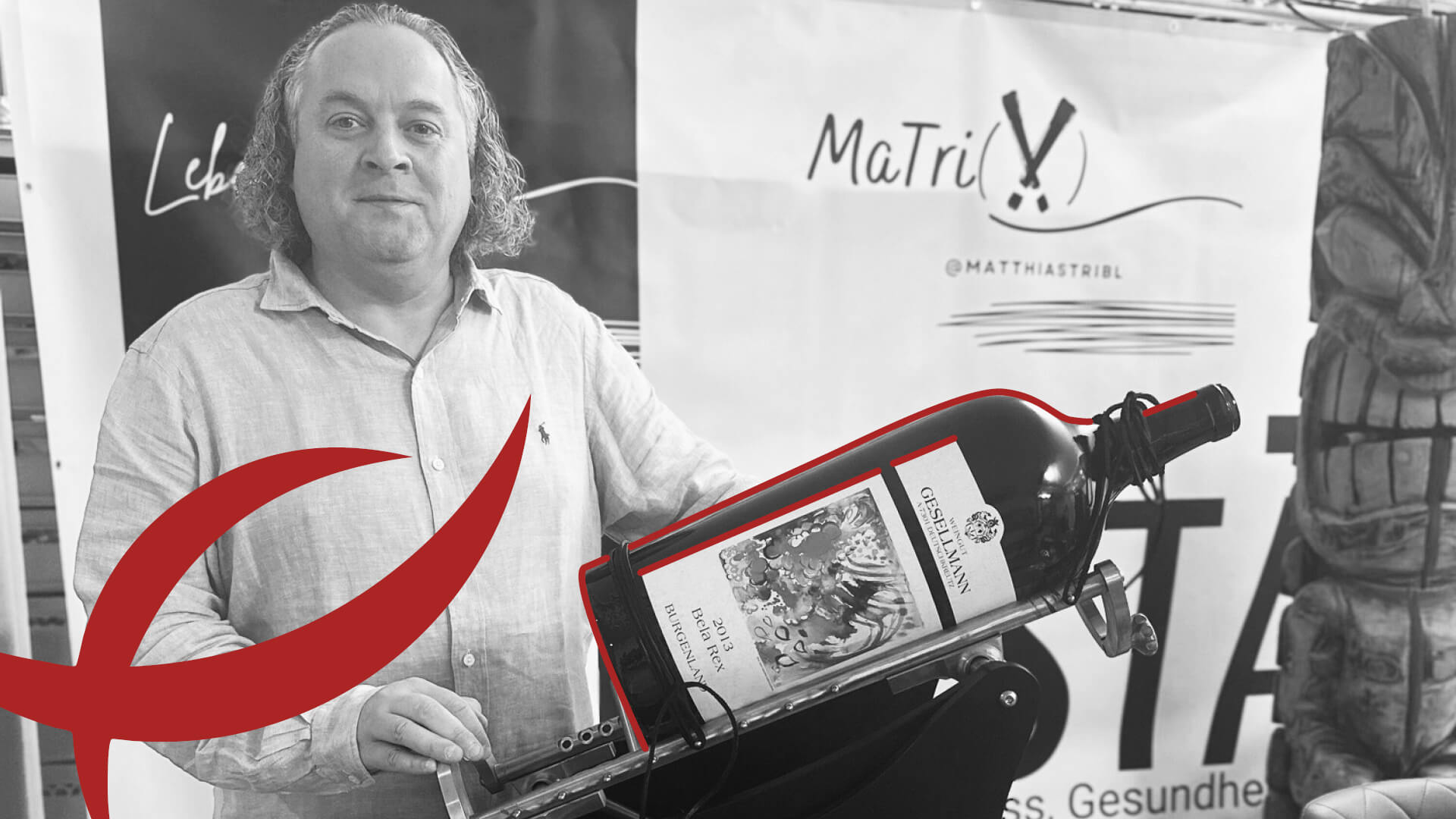 Der Dekanter Herr Tribl in hellem Hemd präsentiert große Weinflasche des Weinguts Giesellmann in Kipphalterung, vor MaTriX Banner mit rotem grafischem Element.